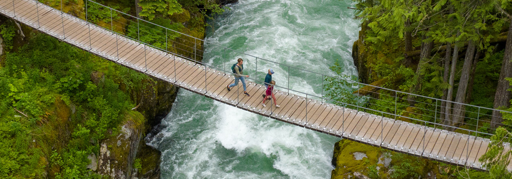 Deux personnes traversant une passerelle au-dessus d’une rivière en forêt illustrant le développement durable et la connexion avec la nature.